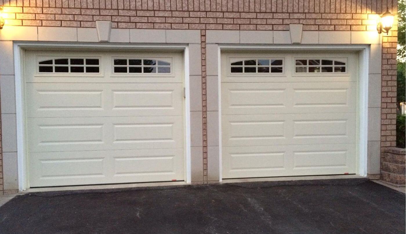 Two white garage doors flanked by lights, creating a welcoming and well-lit entrance to a residential property.