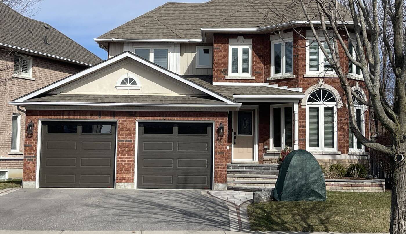 A large house featuring two garages and a spacious driveway, showcasing a well-maintained exterior.